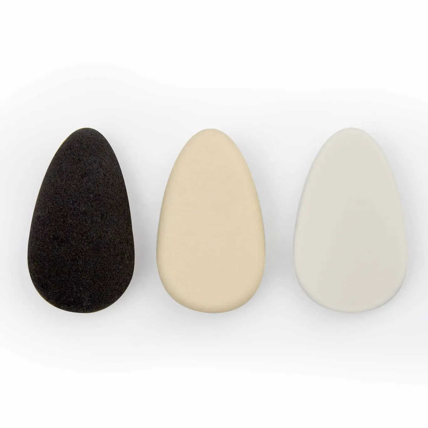 Drei Make-up-Schwämme in Schwarz, Beige und Weiß auf weißem Hintergrund.