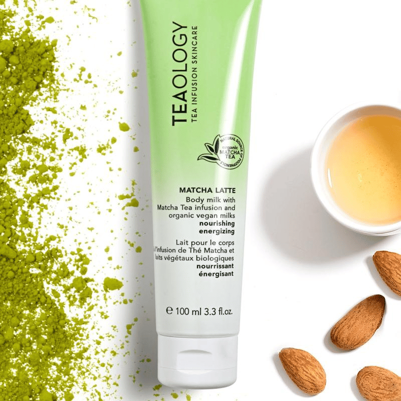 TEAOLOGY Matcha Latte Body Milk 100ml Tube, umgeben von Matcha-Pulver, Mandeln und einer Tasse Tee.