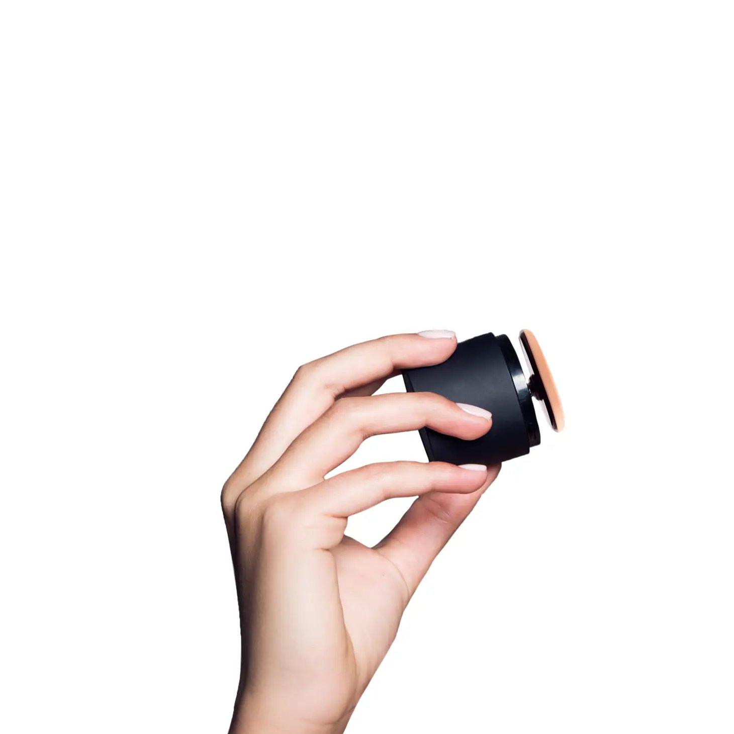 121342B5-1F19-4569-B08F-83E924F69CDA Hand hält ein schwarzes, rundes Kosmetikgerät vor weißem Hintergrund.