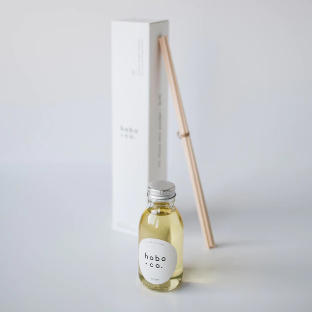 Kleine Flasche mit Duftöl von hobo & co. und Holzstäbchen vor weißem Hintergrund.