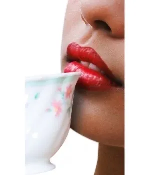 Nahaufnahme von roten Lippen, die an einer weißen Teetasse mit Blumenmuster nippen.