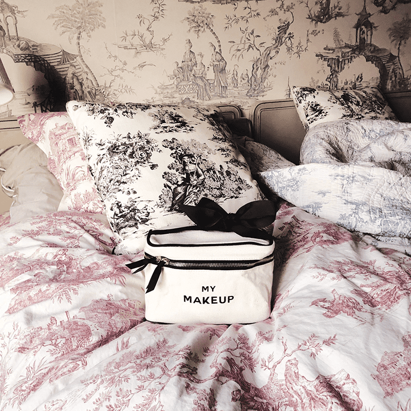 Make-up-Tasche auf einem Bett mit gemusterten Kissen und Decken.