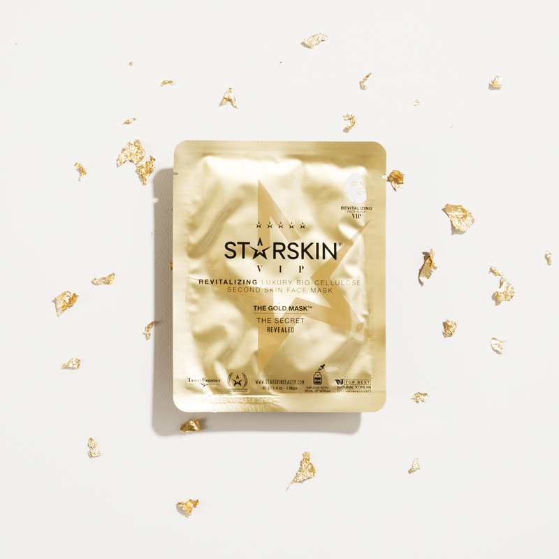 STARSkin VIP The Gold Mask, luxuriöse Gesichtsmaske in goldener Verpackung, umgeben von goldenen Flocken auf weißem Hintergrund.