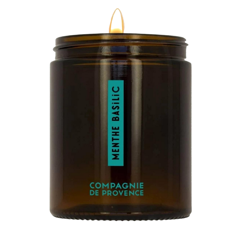 SCENTED-CANDLE-150G-MINT-BASIL Braune Duftkerze in Glas mit Aufschrift 'Menthe Basilic' und 'Compagnie de Provence', brennend.