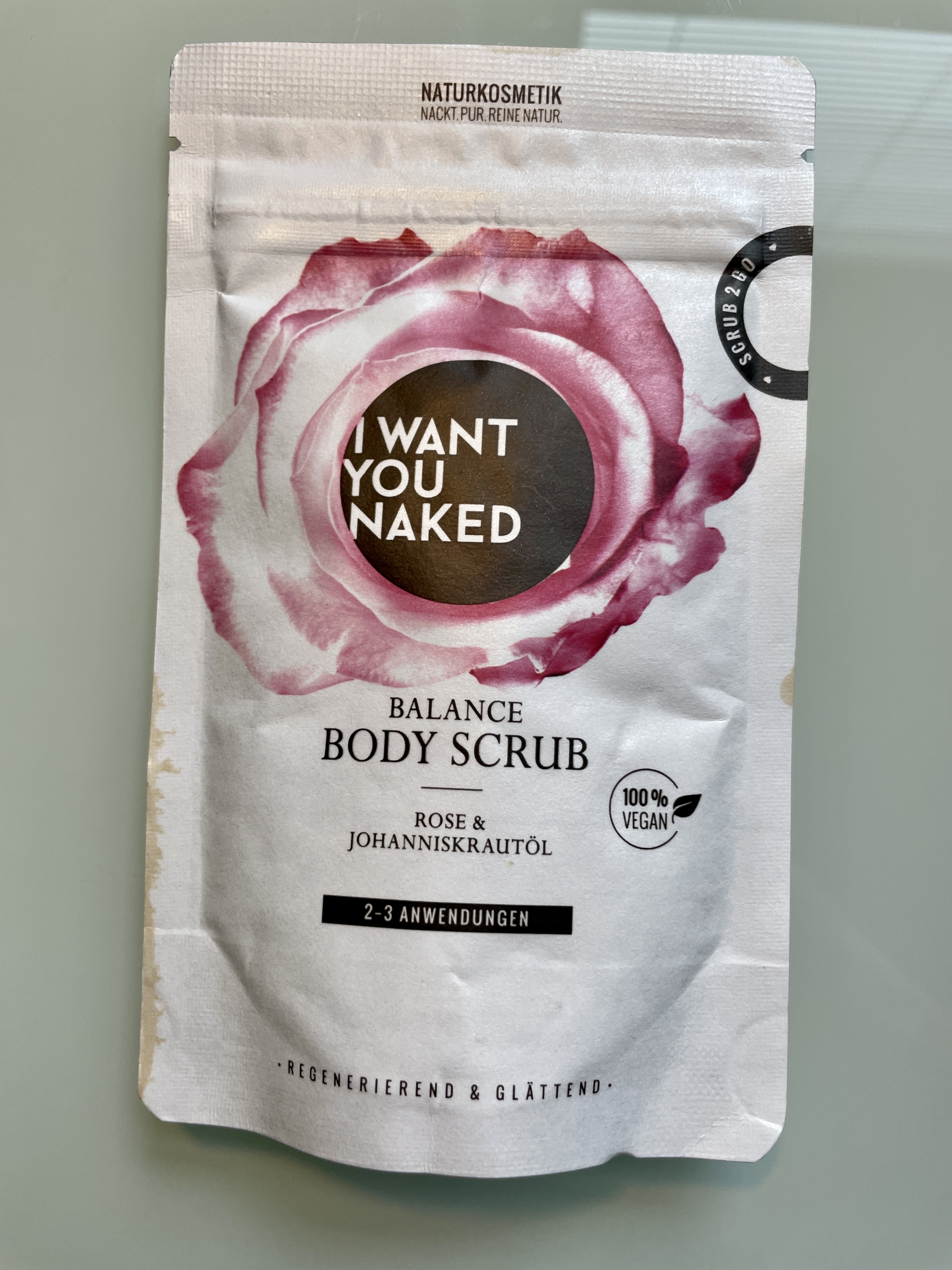 Verpackung von 'I Want You Naked' Balance Body Scrub, Rose & Johanniskraut, 100% vegan, 2-3 Anwendungen, auf einem Tisch.